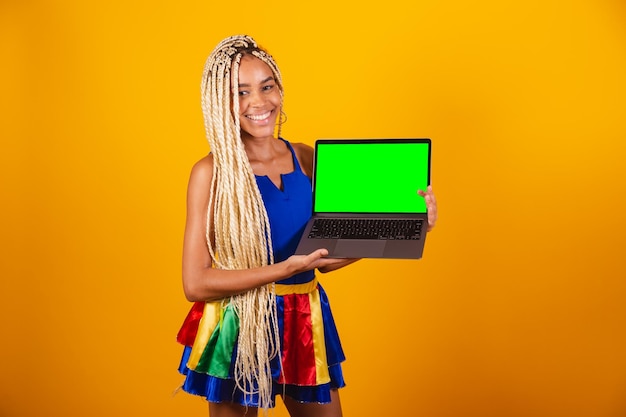 Beautiful black brazilian woman with braids wearing clothes for carnival holding notebook showing green screen of chroma