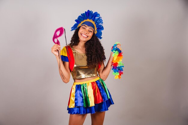 Beautiful black brazilian woman with frevo clothes carnival in\
carnival feather headdress with carnival mask and necklace in\
hands