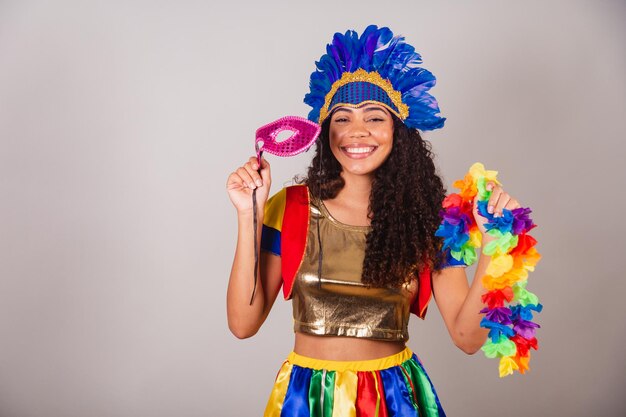 Beautiful black brazilian woman with frevo clothes carnival in\
carnival feather headdress with carnival mask and necklace in\
hands