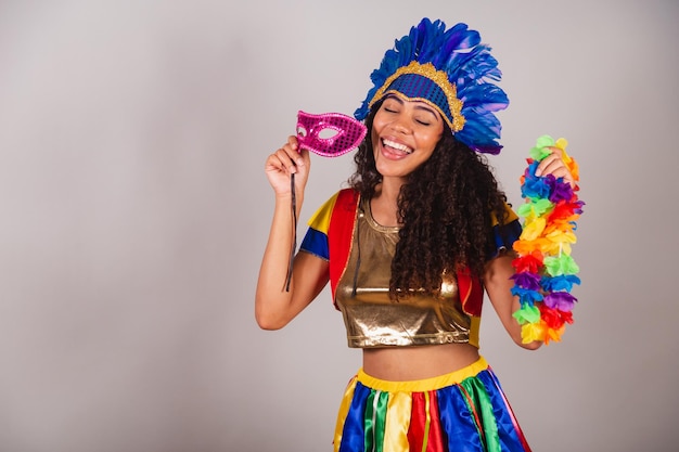 Beautiful black brazilian woman with frevo clothes carnival in\
carnival feather headdress with carnival mask and necklace in\
hands