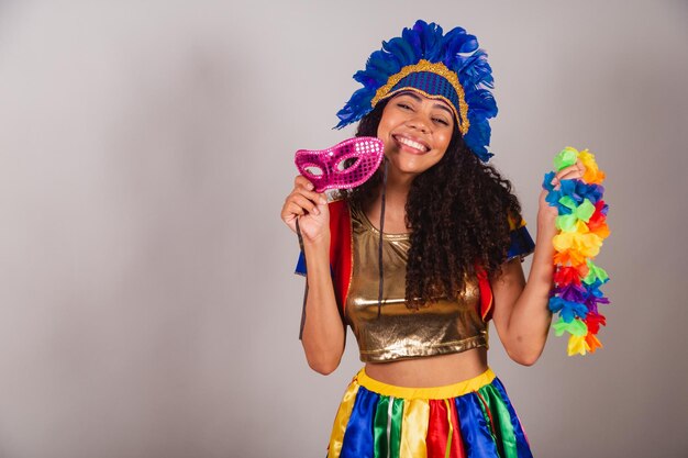 Beautiful black brazilian woman with frevo clothes carnival in\
carnival feather headdress with carnival mask and necklace in\
hands