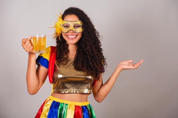 Beautiful black Brazilian woman with frevo clothes carnival wearing a mask dancing with a glass of beer partying in a bar