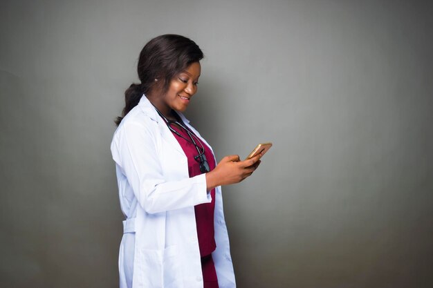 Beautiful black female intern doctor making phone call looking\
at mobile phone screen messaging