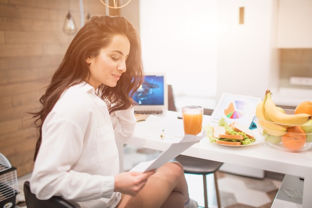 Beautiful black-haired woman works from home. An employee sits in the kitchen and has a lot of work on a laptop and tablet and has video conferencing and meetings.