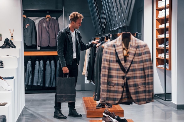 В красивой черной куртке Молодой парень в современном магазине с новой одеждой Элегантная дорогая одежда для мужчин