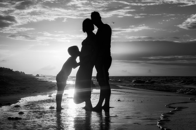 Beautiful black-white shot of a family standing on the coast during sunset time