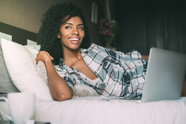 Beautiful black woman on bed with laptop and cup of coffee