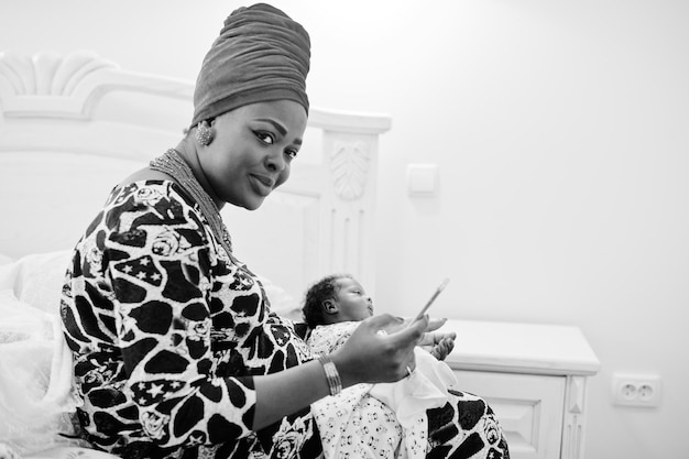 Beautiful black woman in ethnic clothing holding little baby black and white photo