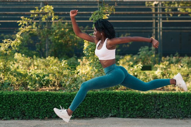 Beautiful black woman running at full speed, jumping and preparing to train in the city