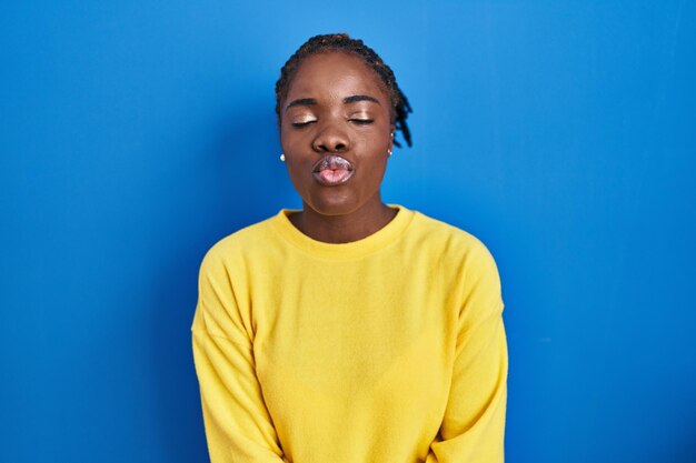 Beautiful black woman standing over blue background looking at the camera blowing a kiss on air being lovely and sexy. love expression.