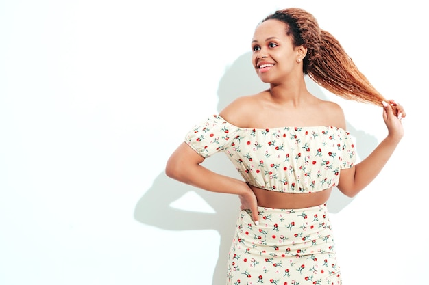 Beautiful black woman with afro curls hairstyle Smiling model dressed in white summer dress Sexy carefree female posing near wall in studio Tanned and cheerful Isolated