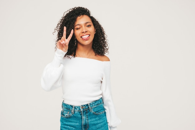 Bella donna di colore con l'acconciatura di riccioli afro. modello sorridente in maglione e vestiti di jeans alla moda