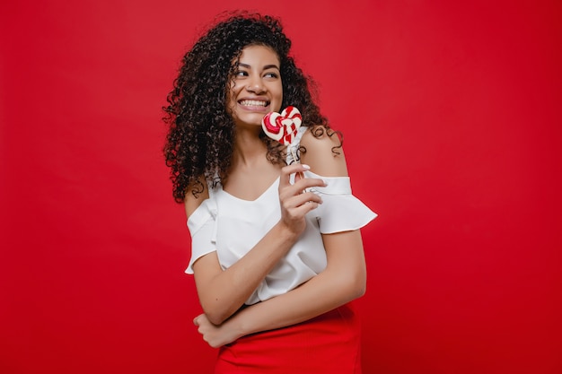 Beautiful black woman with heart shaped lollypop candy on red wall