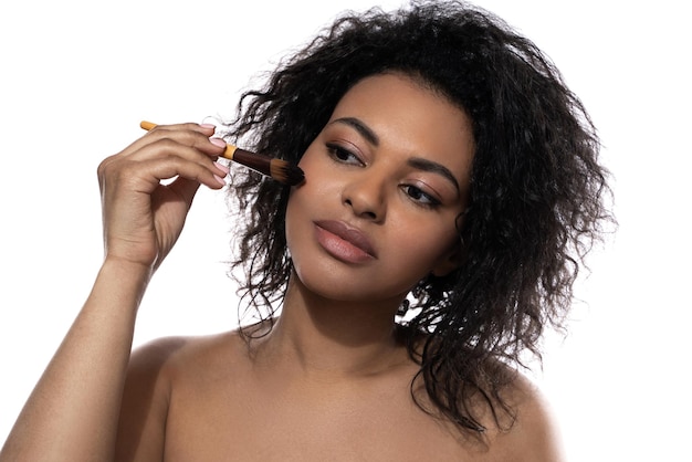 Красивая черная женщина с гладкой кожей с помощью кисти для макияжа на белом фоне