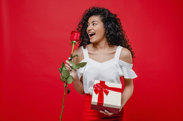 Beautiful black woman with valentine gift and rose isolated over red