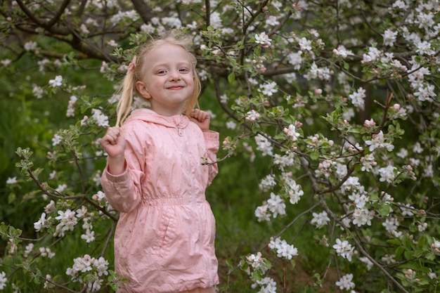 Beautiful blond girl in blooming garden enjoy spring day Small girl in pink outfit near flowering tree