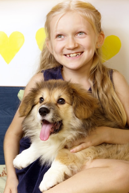 カメラを見ている美しいブロンドの女の子とコーギーふわふわの子犬