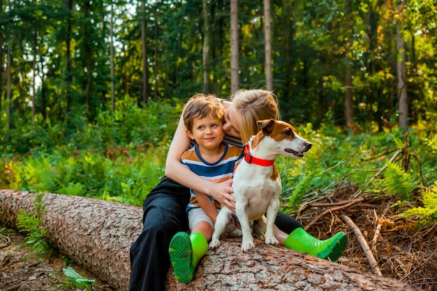 Beautiful blond hair mothe sits on log with son and a dog in the forest