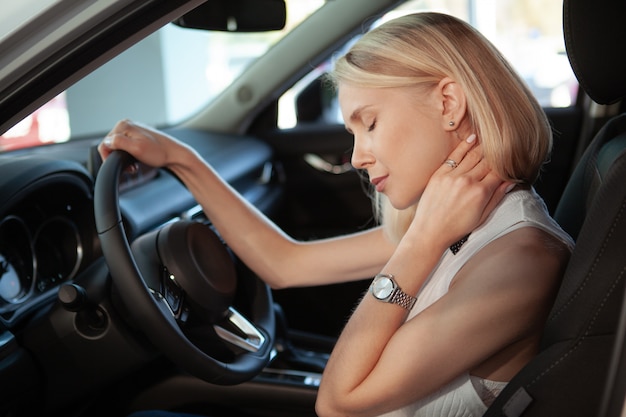 Beautiful blond haired woman rubbing her aching neck, sitting in her car.