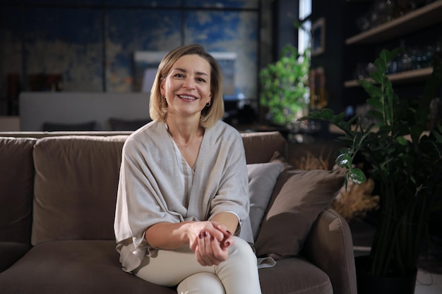 Beautiful blond middle aged woman relaxing sitting on sofa.