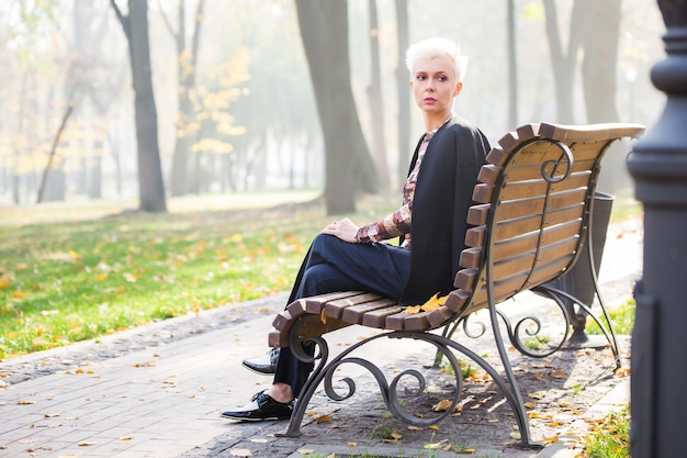 Beautiful blond stylish woman in autumn park on the bench