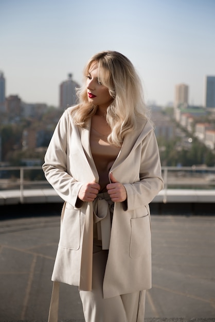 Beautiful blond woman in beige coat standing on the roof top of the house.