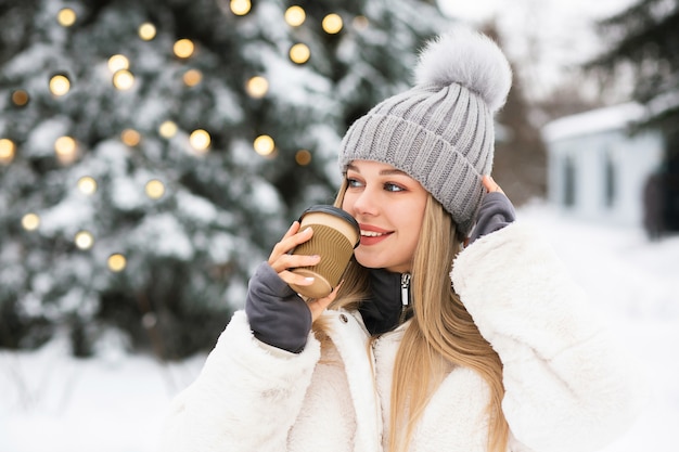 冬の公園でコーヒーを楽しんでいる美しいブロンドの女性。空きスペース