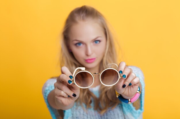 Beautiful blond woman holding sunglasses on yellow background focus on the glasses