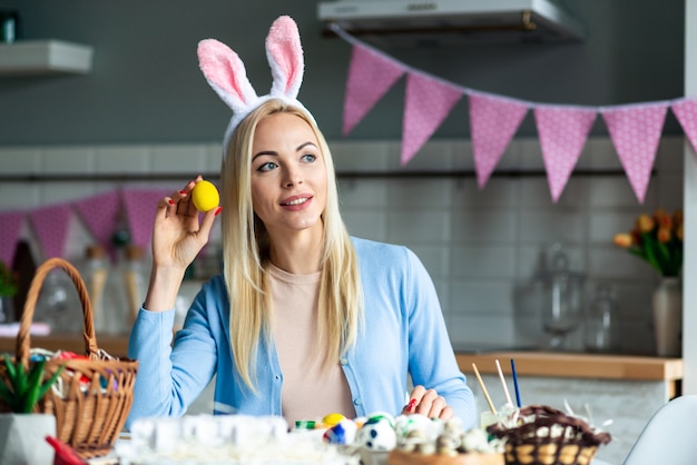 Beautiful blond woman holds an Easter egg in her hand and looks away dreamily.