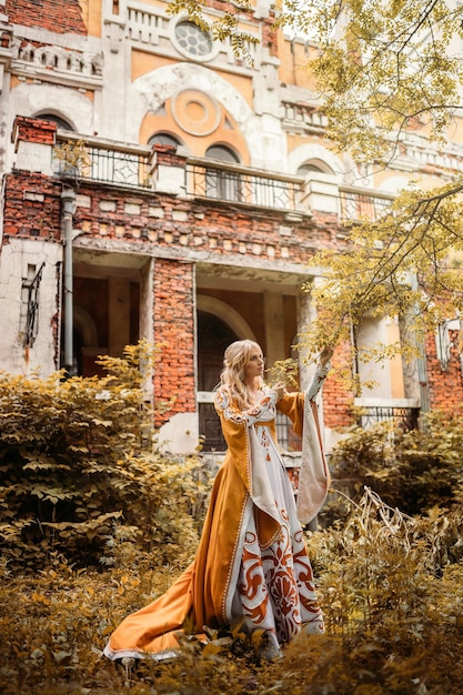 Красивая белокурая женщина в средневековом платье гуляет возле старого здания