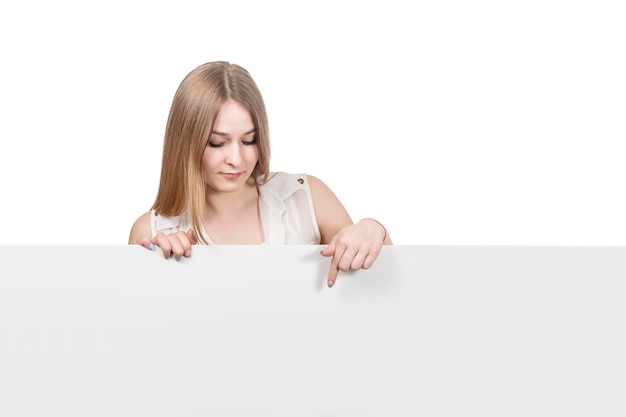 beautiful blond woman points finger down on a blank board isolated on white background