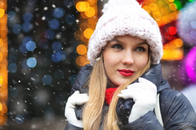 Beautiful blond woman wears knit cap walking at the winter fair during snowfall. Empty space for text