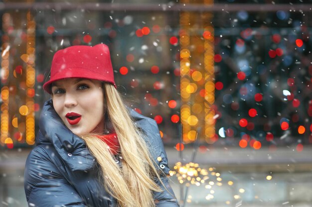 Beautiful blond woman wears red hat playing with bengal lights at the holiday fair. Space for text