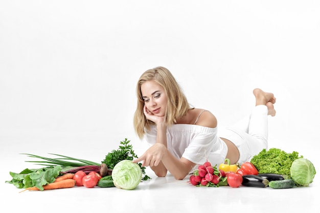 Bella donna bionda in abiti bianchi e un sacco di verdure fresche su uno sfondo bianco