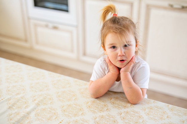 Beautiful blonde baby girl having breakfast in kitchen. Funny faces