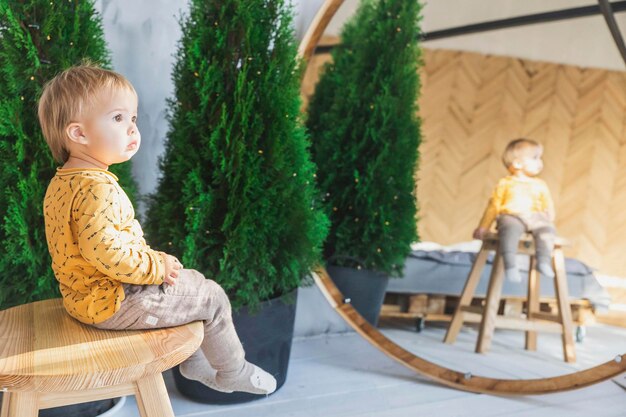 Foto bellissimo bambino biondo seduto su uno sgabello in camera da letto vicino allo specchio