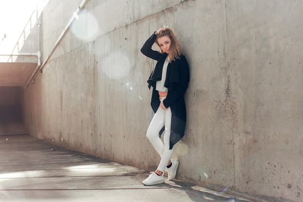 Photo beautiful blonde in a black cape posing against the a concrete wall