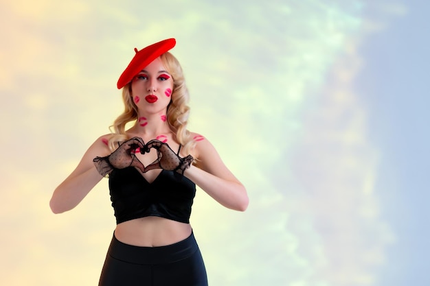 Beautiful blonde in black leather pants and top red hat black lace gloves Traces of kisses on the body and face Shows a heart with his hands and a kiss with his lips Yellow abstract background