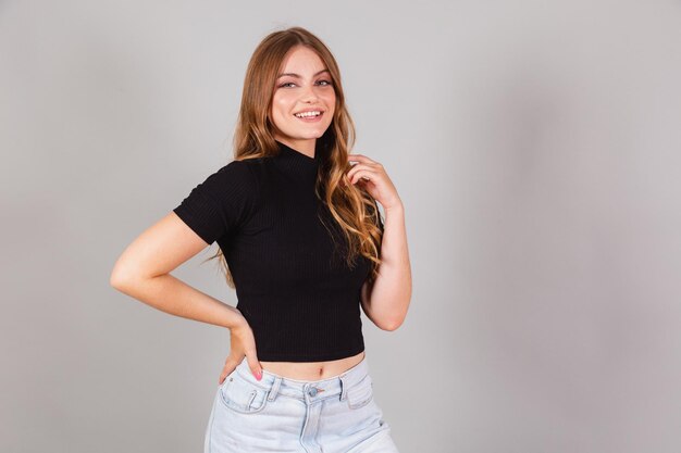 Foto bella donna brasiliana bionda che indossa camicia nera e jeans sorride con la mano nei capelli