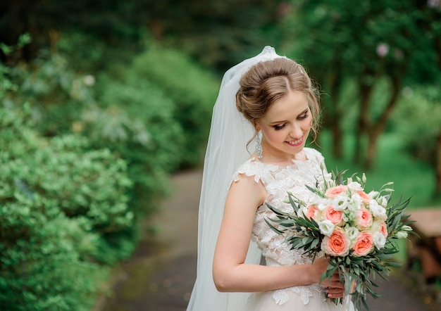 Beautiful blonde bride poses with orange wedding bouquet in the park