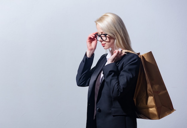 Beautiful blonde businesswoman in suit with shopping bag on gray background