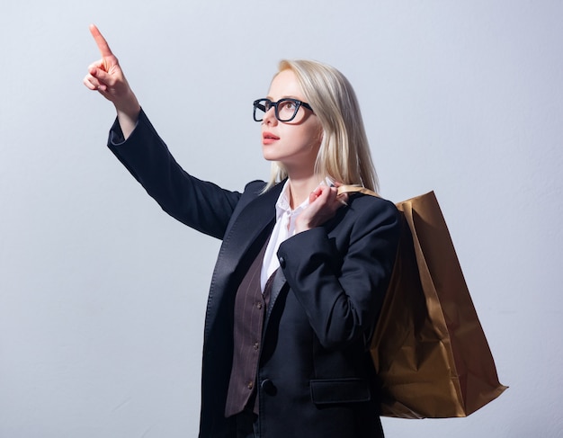 Beautiful blonde businesswoman in suit with shopping bag on gray background