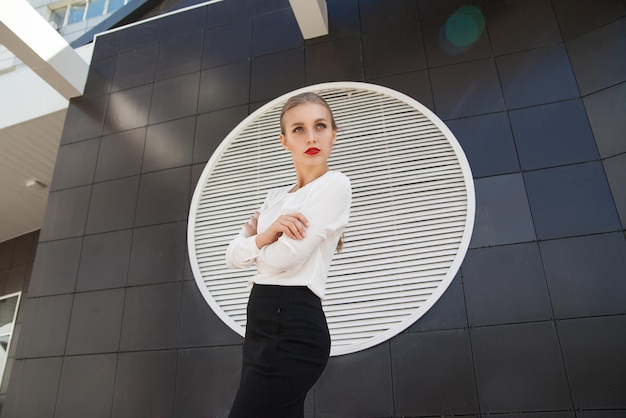 Beautiful blonde businesswoman with red lips looking away against of building wall
