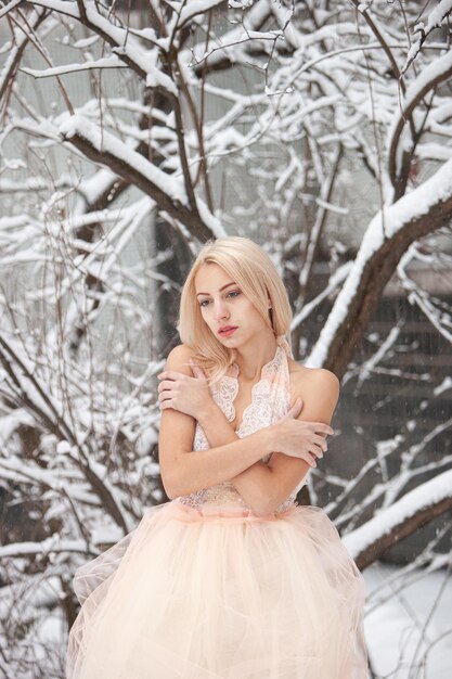 A beautiful blonde in a chic pink dress against the backdrop of a snowcovered park