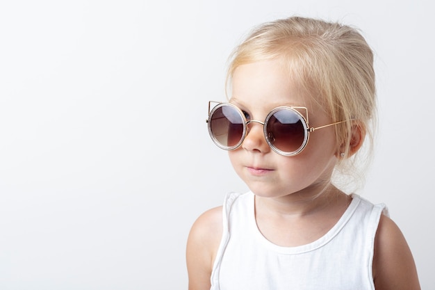 Beautiful blonde child in sunglasses on a light studio background.