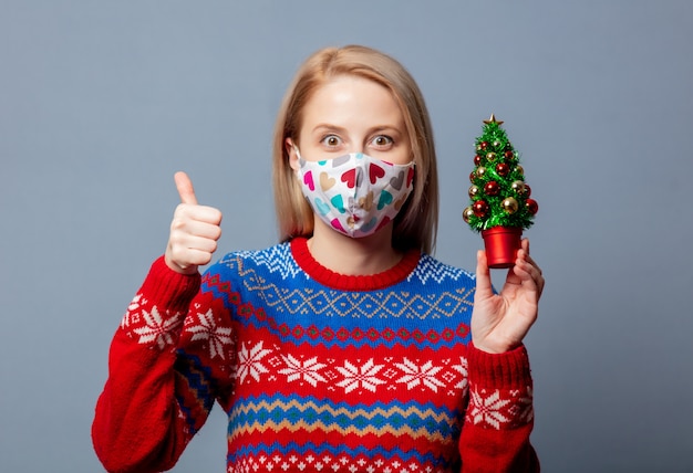 Foto bella bionda in maglione di natale con alberello su gray