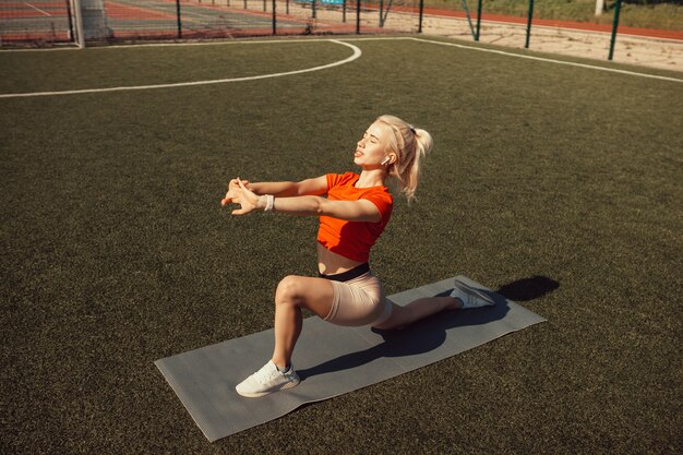 Beautiful blonde doing stretching on the lawn of a football field