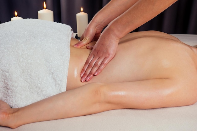 Beautiful blonde female relaxation in spa salon with professional masseur shoulder body next to the candle fire