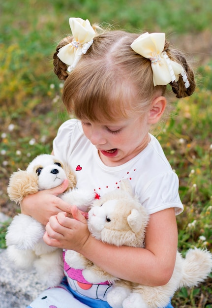 a beautiful blonde girl of 4 years old, in light clothes and light bows, hugs soft toys and looks at them emotionally