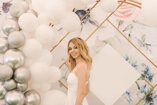 Beautiful blonde girl on the background of a round photo zone with white balls for an event or birthday